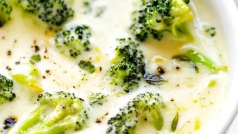 Bowl of deliciously cheesy broccoli cheese soup garnished with fresh herbs