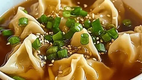 A steaming bowl of cozy wonton soup with savory dumplings and fresh herbs.