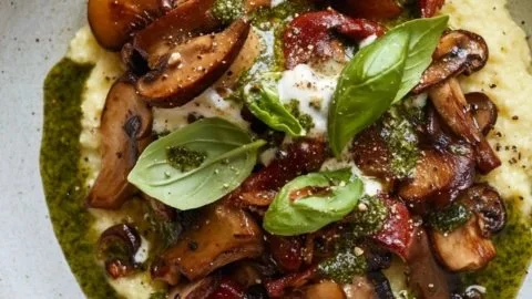 Creamy polenta with sautéed mushrooms and basil vinaigrette served on a plate.