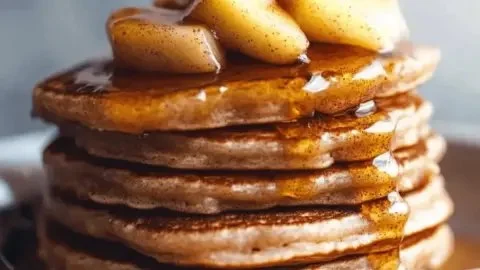 Fluffy apple cinnamon pancakes topped with syrup and apples, a fall breakfast delight.