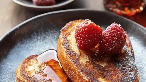 Delicious French toast topped with fresh fruit and syrup on a plate