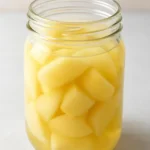 A jar of pickled ginger slices with fresh ginger root
