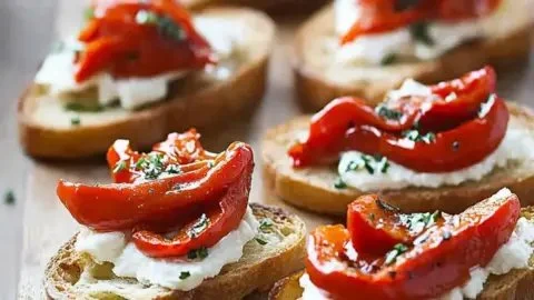 Roasted red peppers goat cheese crostini with fresh herbs on a platter