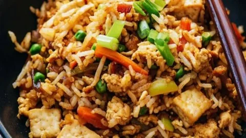 A plate of crispy tofu fried rice garnished with green onions and peppers